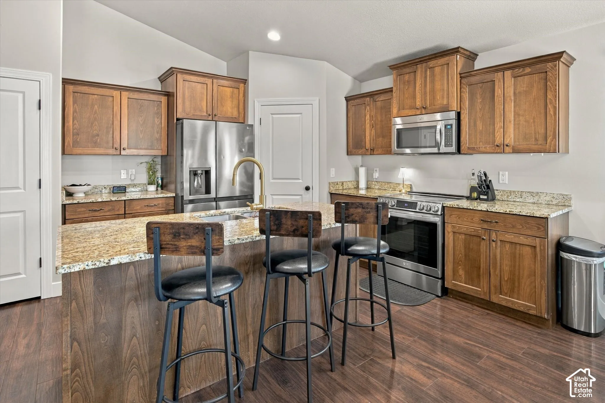 Kitchen featuring wood-finish flooring, granite countertops, wood cabinetry, and stainless steel appliances including a refrigerator, range, and microwave