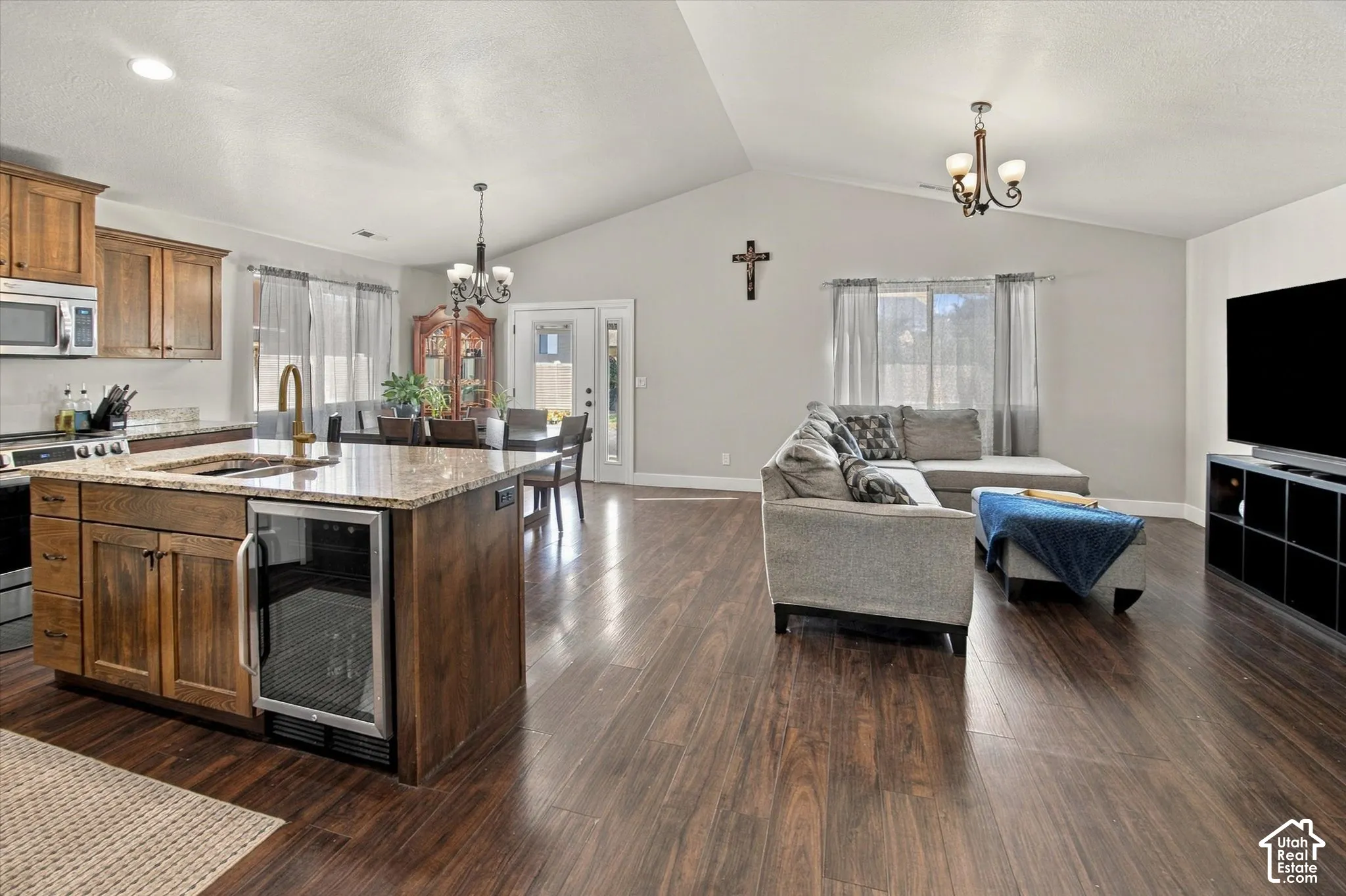 Open-concept living space featuring vaulted ceilings, wood-finish flooring, a kitchen island with stone countertops, and built-in stainless steel appliances