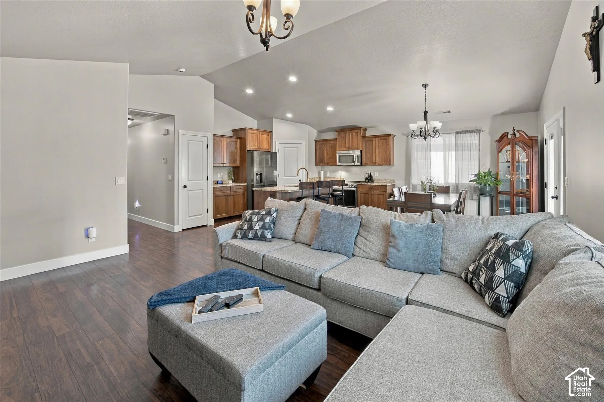 Open concept living area with wood-finish flooring, vaulted ceiling, recessed lighting, and a kitchen featuring wood cabinetry and stainless steel appliances