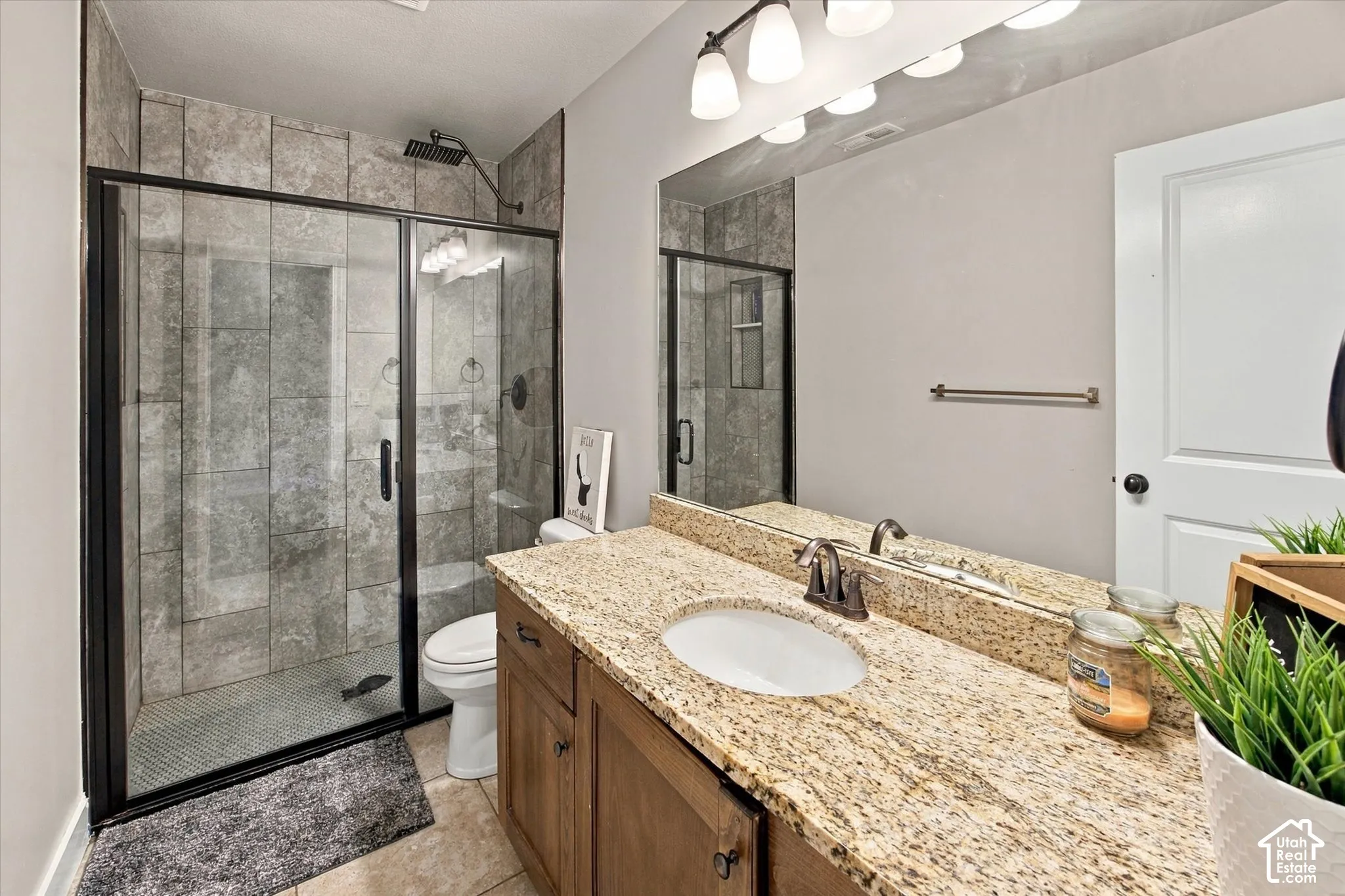 Walk-in shower with tiled surround and black-framed glass enclosure, vanity with granite countertop, integrated basin, and bronze-finish faucet