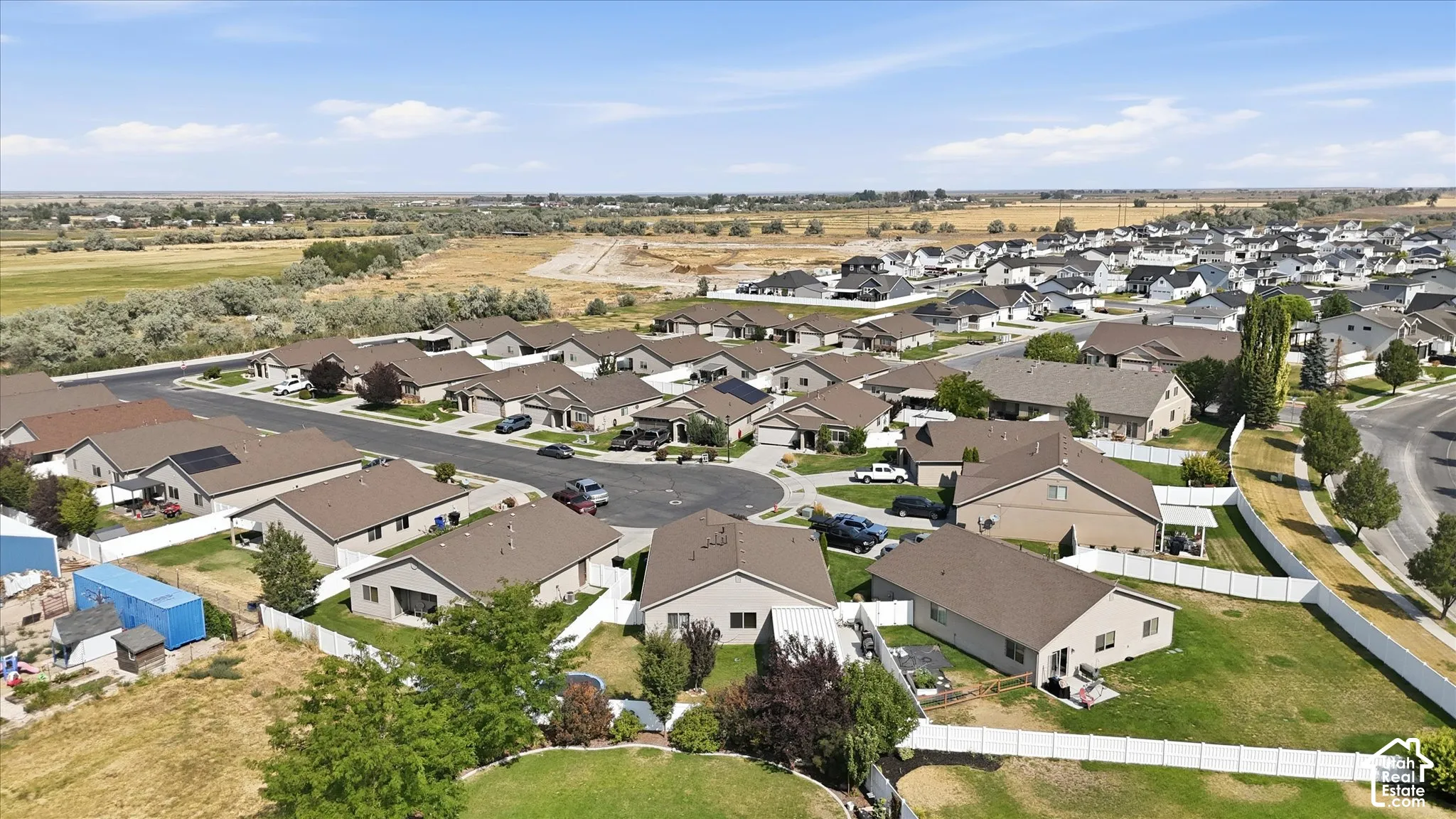 Residential neighborhood featuring single-story homes with brown roofs, cul-de-sac streets, a white perimeter fence, and open fields in the background