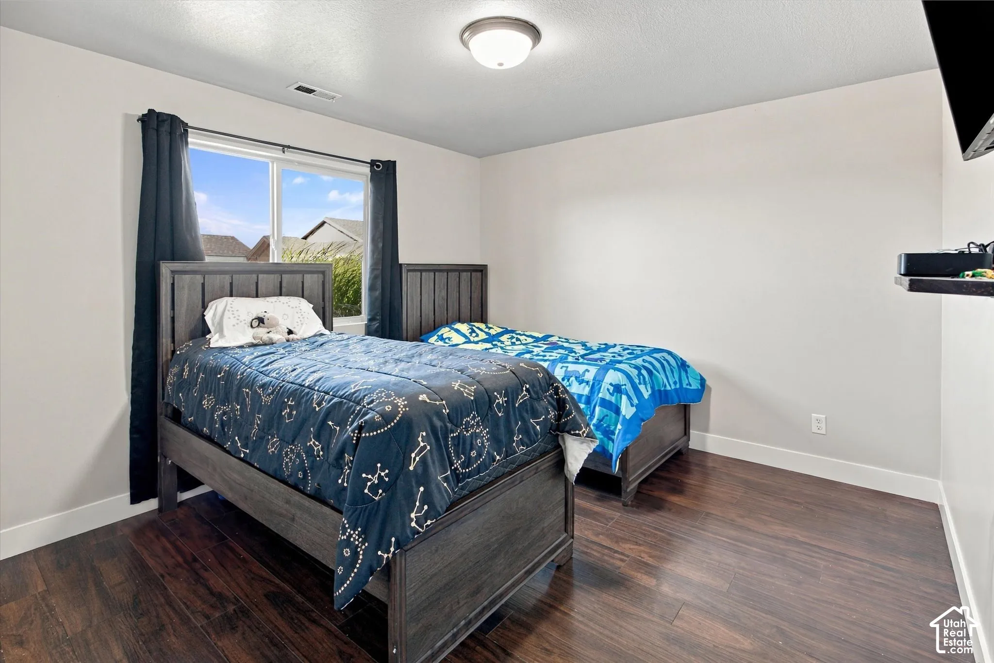 Wood-finish flooring with white baseboards, a window with dark curtains, and a ceiling-mounted light fixture