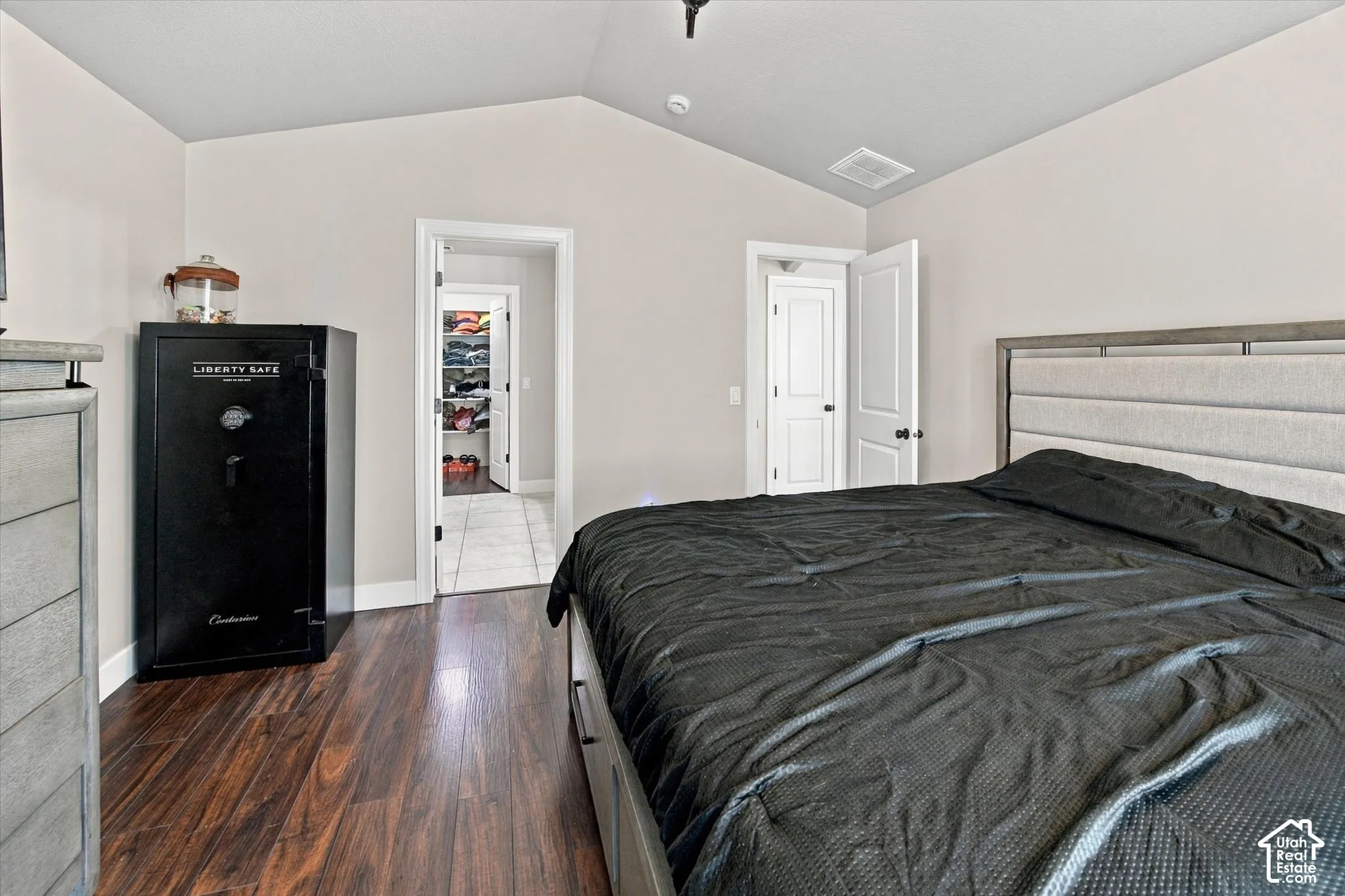 Vaulted ceiling, wood-finish flooring, white paneled doors, and an open doorway to a tiled space