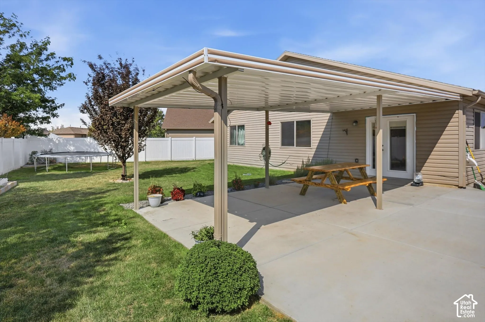 Backyard featuring a covered patio, concrete slab, and a green lawn with mature trees