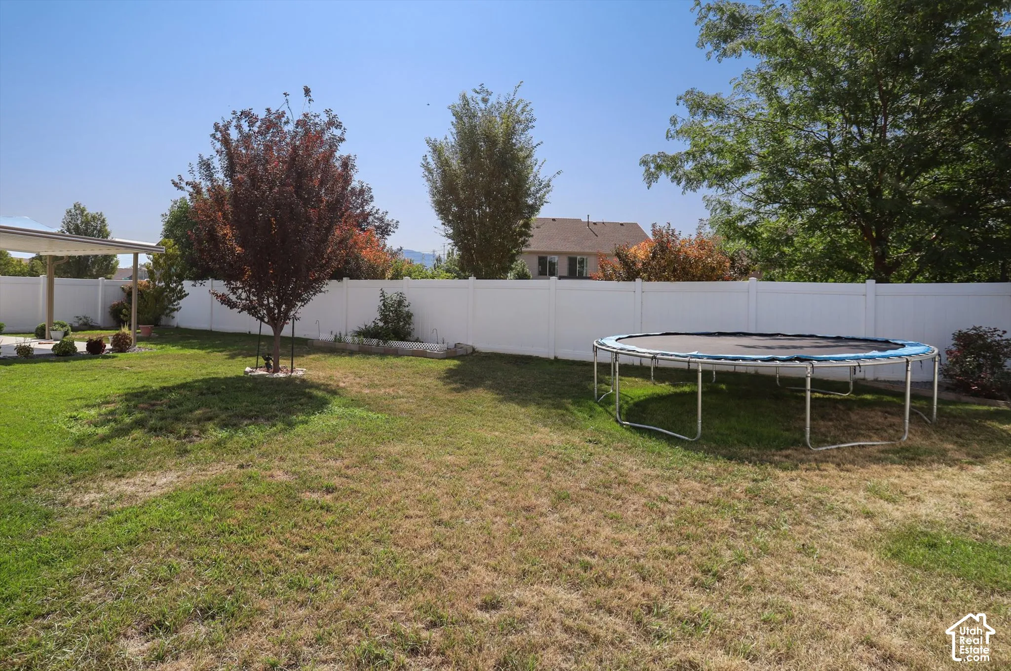 Spacious backyard with a white privacy fence, mature trees, and a covered patio structure