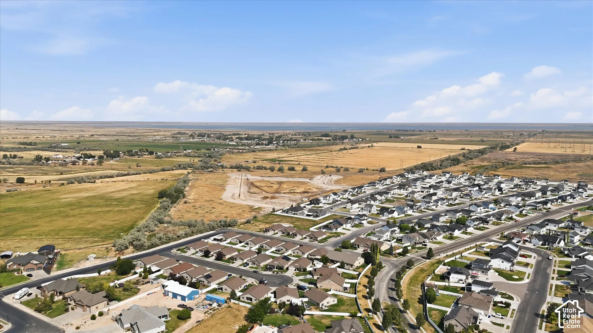 Expansive aerial perspective showcasing a residential neighborhood with varied architectural styles, paved streets, and a mix of developed and undeveloped land