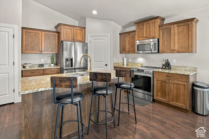 Kitchen featuring wood-finish flooring, granite countertops, wood cabinetry, and stainless steel appliances including a refrigerator, range, and microwave