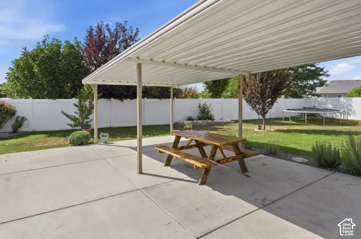 Expansive concrete patio with a covered pergola, featuring a generous grassy area and surrounding mature greenery