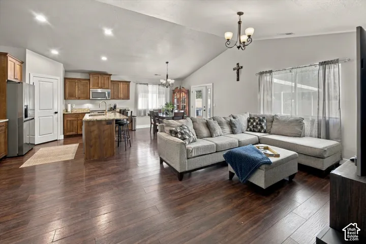 Vaulted ceiling with a chandelier, wood-finish flooring, kitchen island with granite countertop, stainless steel appliances, and wood cabinetry
