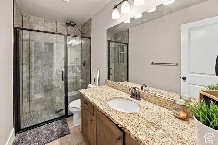 Walk-in shower with tiled surround and black-framed glass enclosure, vanity with granite countertop, integrated basin, and bronze-finish faucet