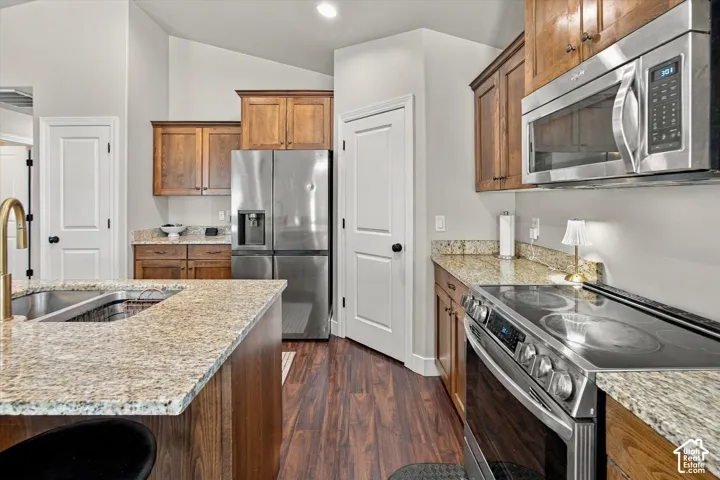Kitchen featuring wood cabinetry, stainless steel appliances, granite countertops, and wood-finish flooring