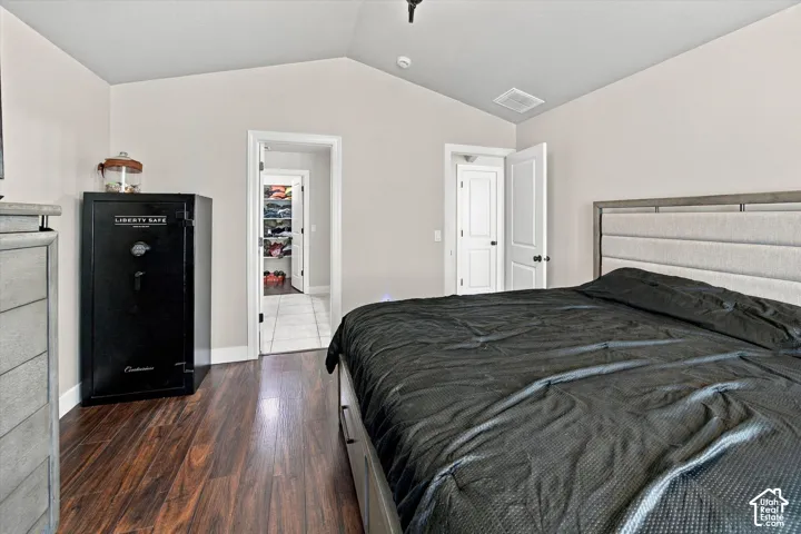 Vaulted ceiling, wood-finish flooring, white paneled doors, and an open doorway to a tiled space
