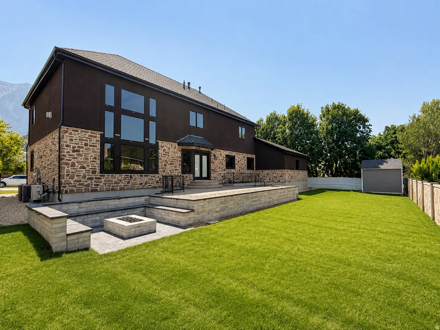 Spacious backyard featuring a large paved patio with built-in seating, a fire pit, and a separate storage shed