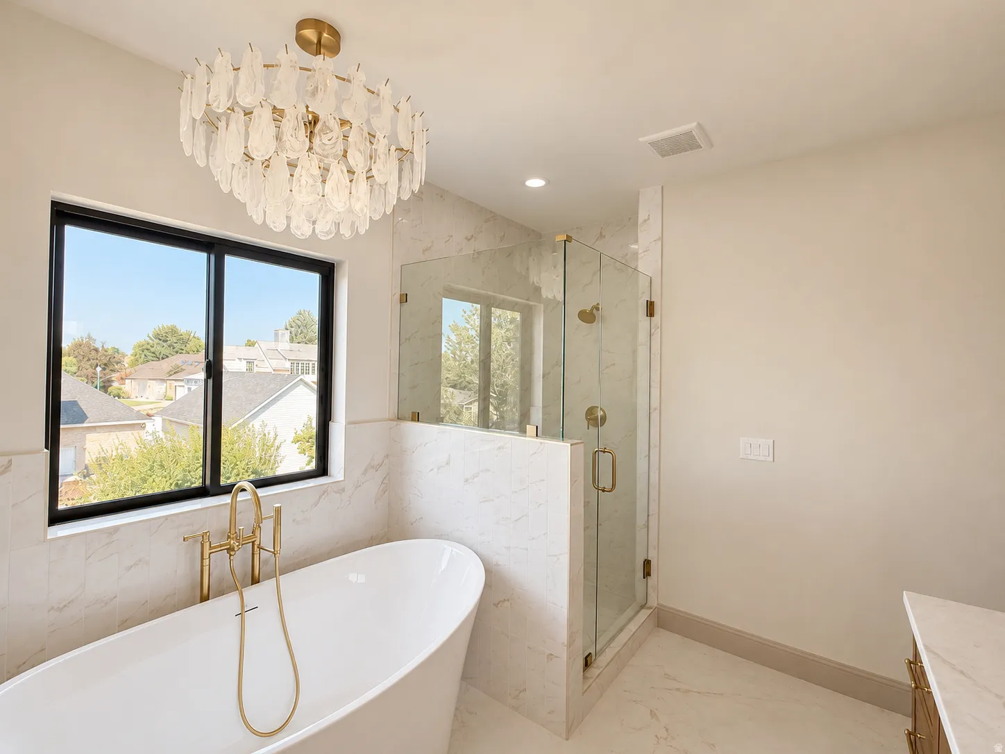 Freestanding soaking tub with a gold-finish filler, walk-in shower with clear glass enclosure and gold-finish fixtures, and a beautiful chandelier