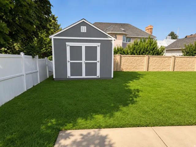 Expansive lawn featuring a storage shed with double doors, a white privacy fence, and a textured privacy wall