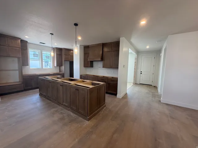 Expansive kitchen featuring a large central island, extensive wood cabinetry, and wood-finish flooring