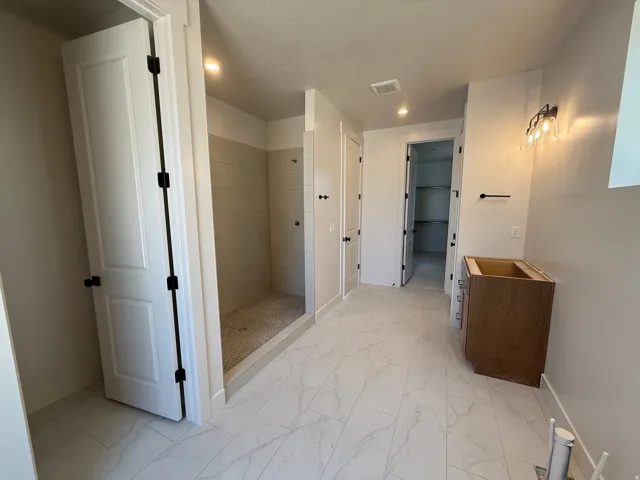 Spacious bathroom with large format tile flooring, a walk-in shower with tile surround, and a pre-installed vanity cabinet base
