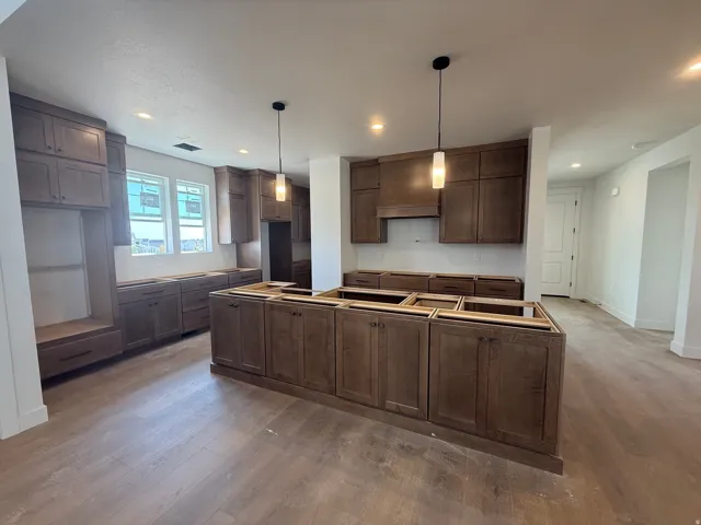 Spacious kitchen featuring extensive wood cabinetry, a large center island, wood-finish flooring, recessed lighting, and modern pendant fixtures