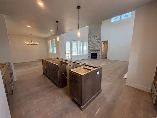 Wood-finish flooring throughout, vaulted ceilings, stone fireplace, recessed lighting, and kitchen island cabinetry