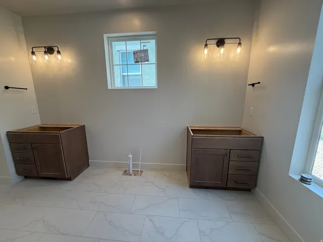 Dual vanity bases with integrated drawers, modern wall-mounted light fixtures, and large-format floor tiling