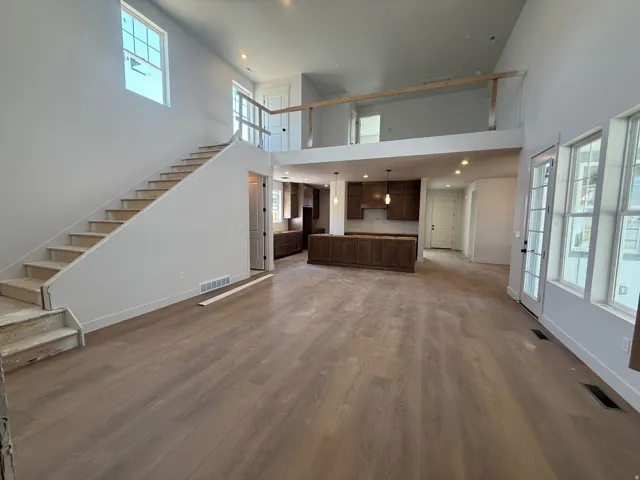 Open concept living area featuring wood-finish flooring, a two-story ceiling, a contemporary kitchen with wood cabinetry, a central island, and a second-story loft with a railing
