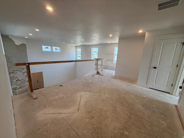 Recessed ceiling lighting illuminates a spacious unfinished room featuring multiple windows, a stone accent wall, and a two-panel interior door with dark hardware