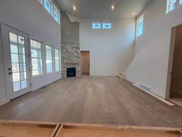 Wood-finish flooring throughout, a stone-clad fireplace with a wood mantel, high ceilings, recessed lighting, and multiple windows
