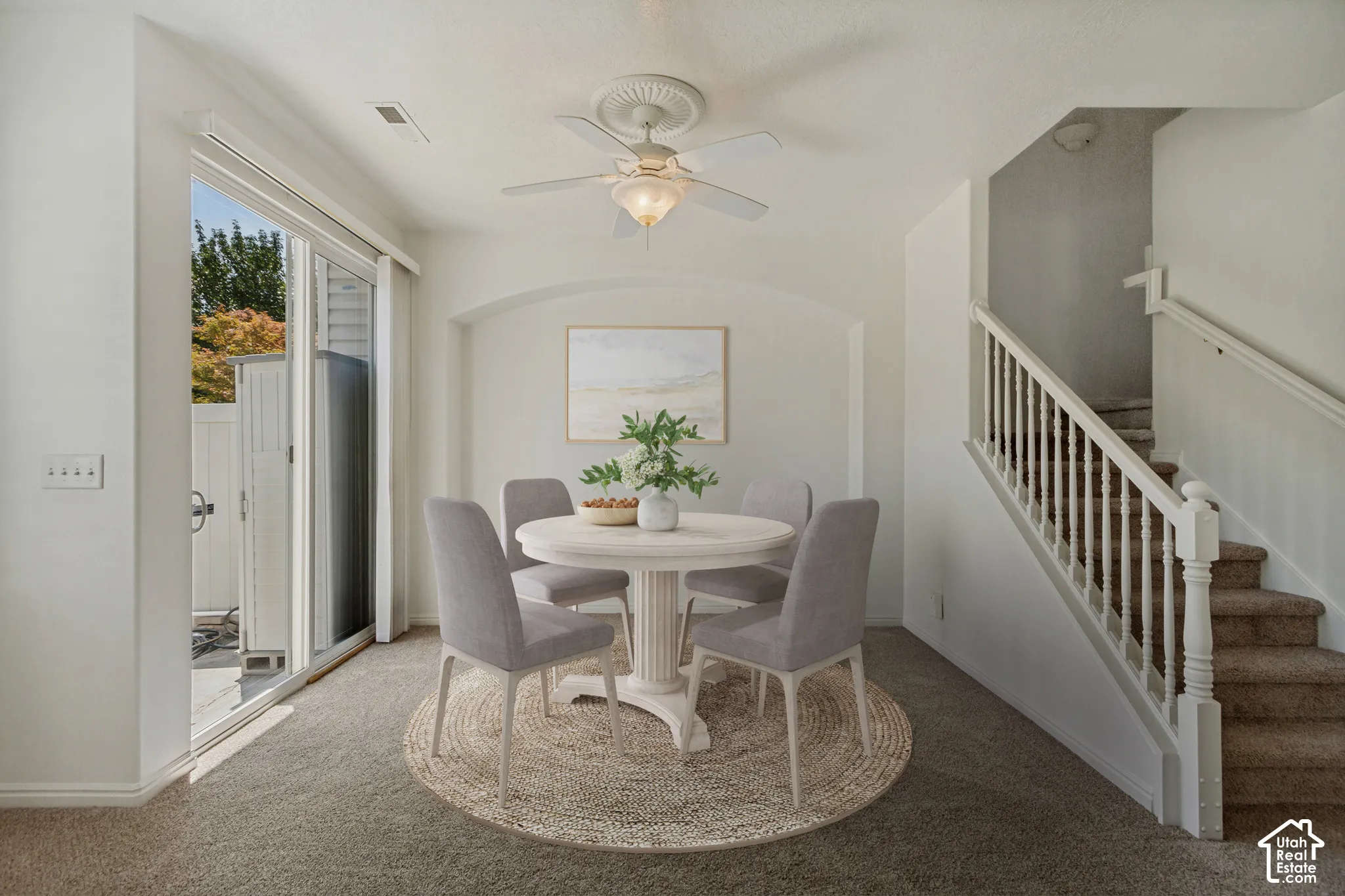Sliding glass door, wall-to-wall carpeting, staircase with white banister, archway, and ceiling fan with integrated lighting