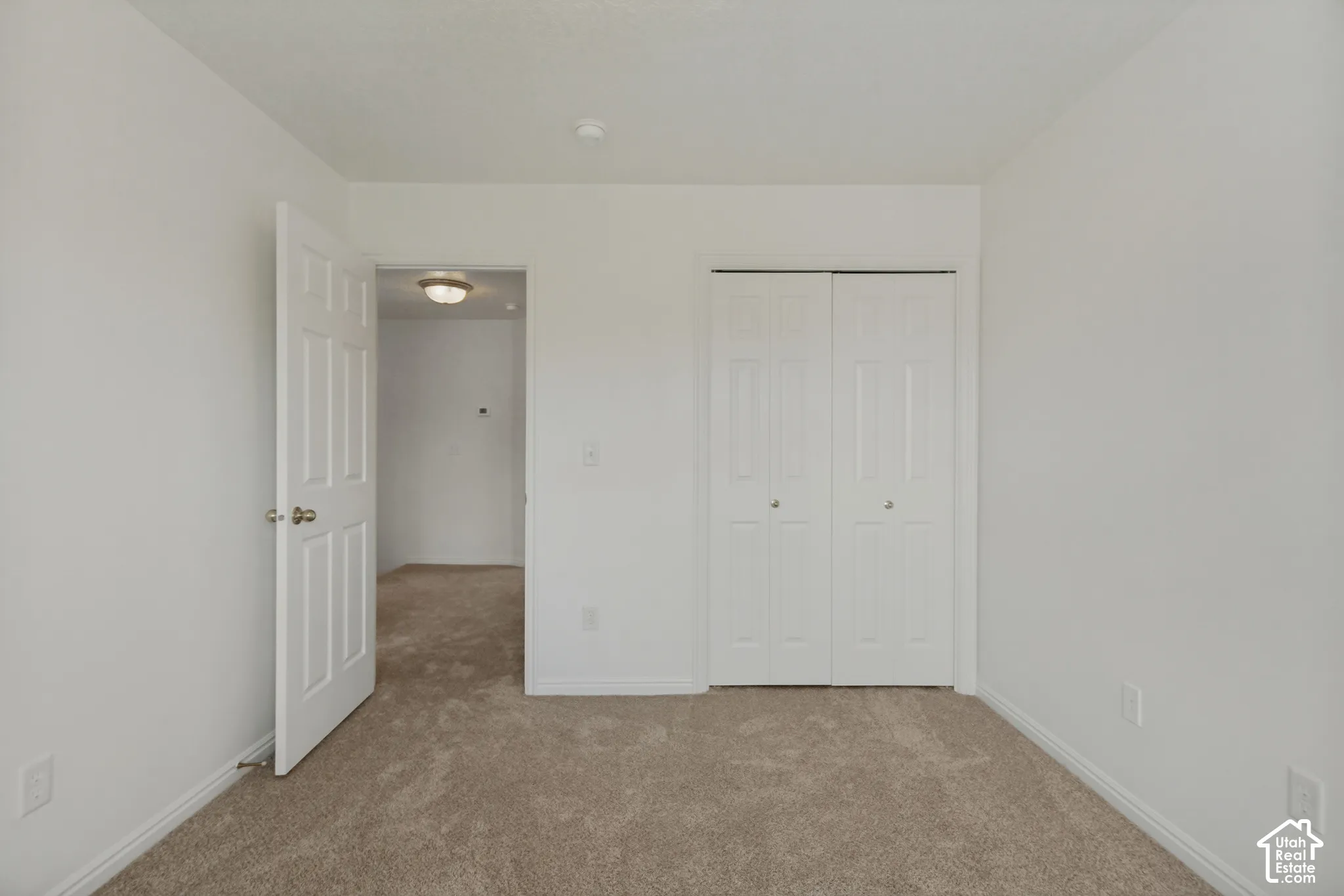 Wall-to-wall carpeting in a neutral tone, white bi-fold closet doors, and a white paneled interior door