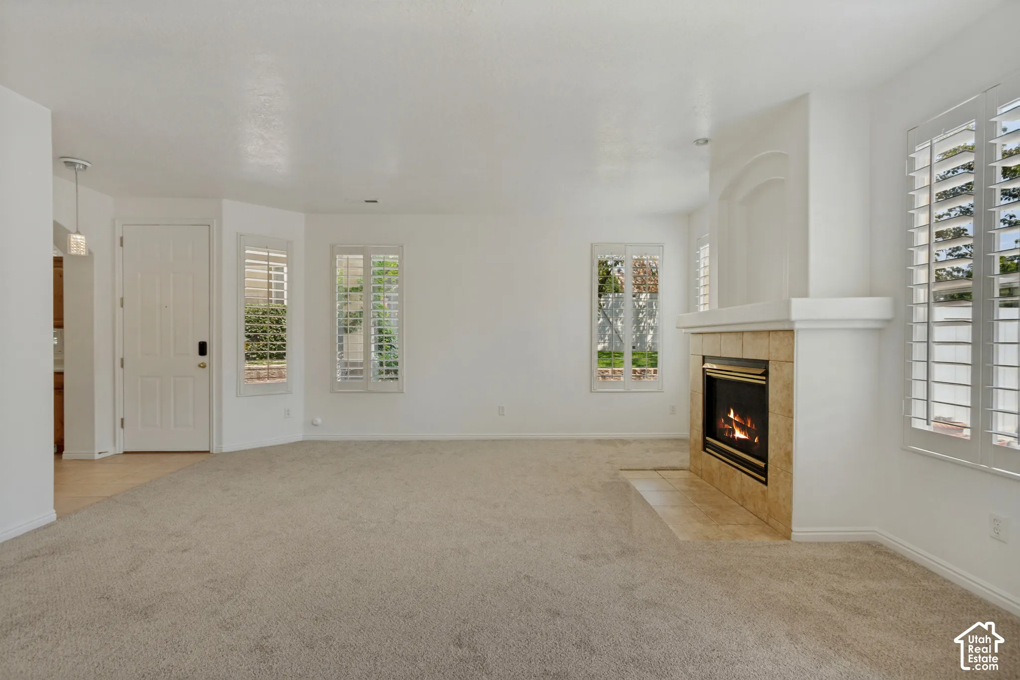 Neutral carpet flooring, fireplace with tile surround, multiple windows with plantation shutters, and a paneled entry door