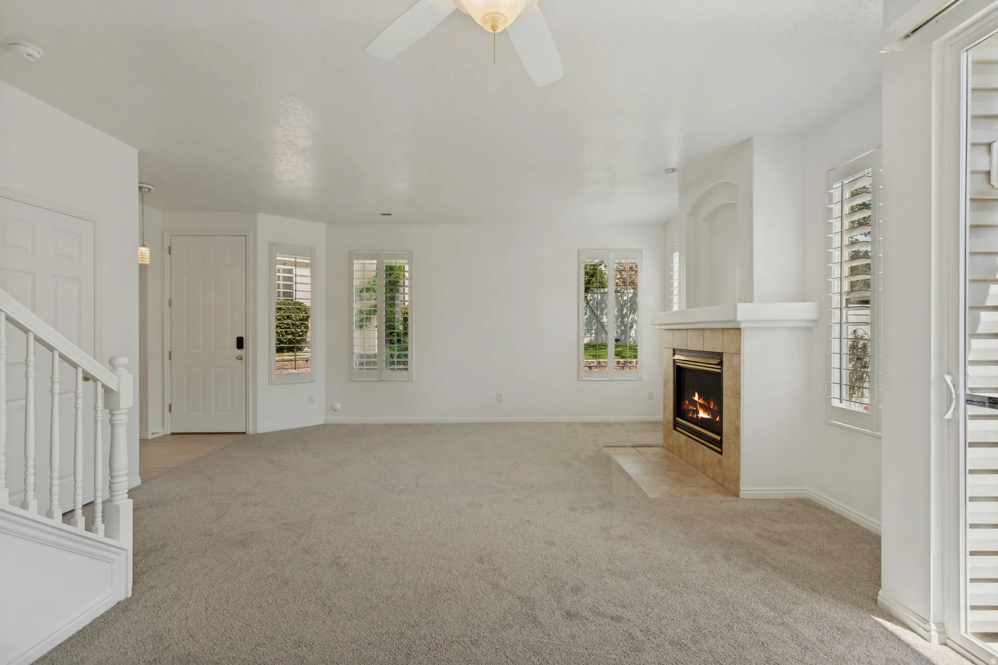 Spacious living area featuring a fireplace with a tile surround, multiple windows with plantation shutters, and a ceiling fan