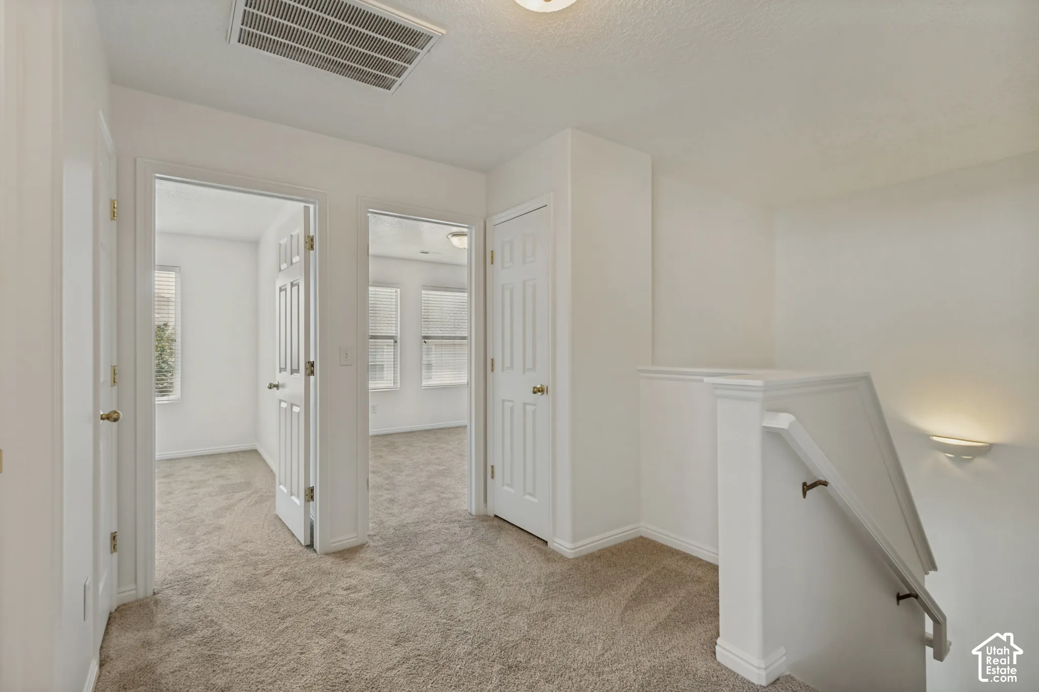 Carpeted hallway with white interior doors, a staircase with a white railing, and a wall-mounted light fixture