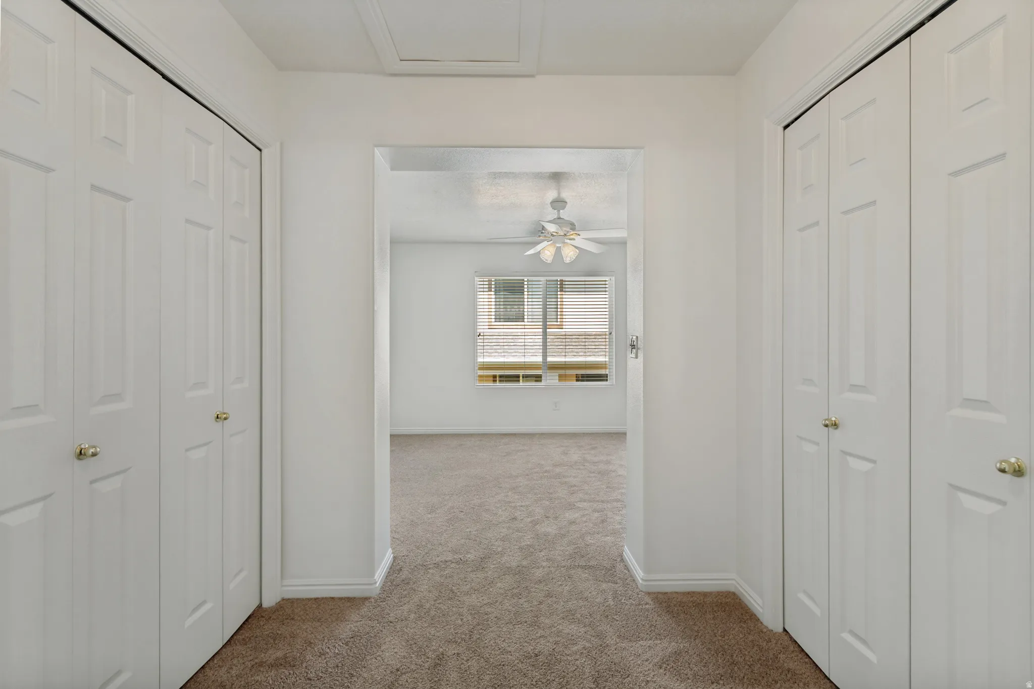 Plush carpet flooring, white bi-fold closet doors, brass door hardware, white window blinds, and a ceiling fan with integrated lighting