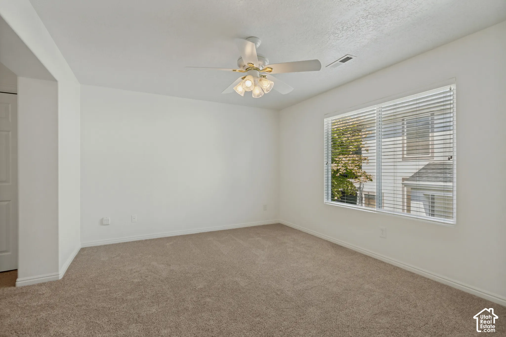 Neutral-toned carpeting, white walls, ceiling fan with integrated lighting, and a large window with blinds