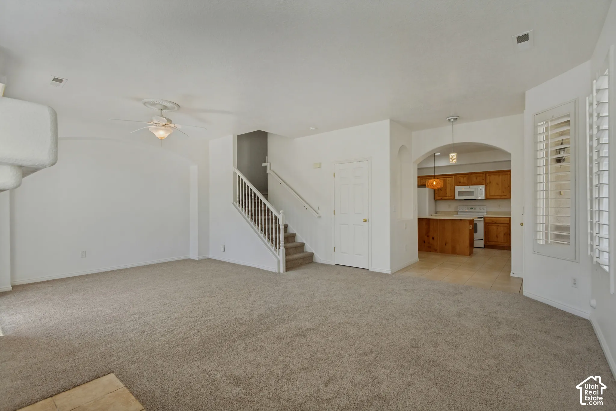 Carpeted living area featuring an architectural fireplace element, ceiling fan, and a staircase with white balusters