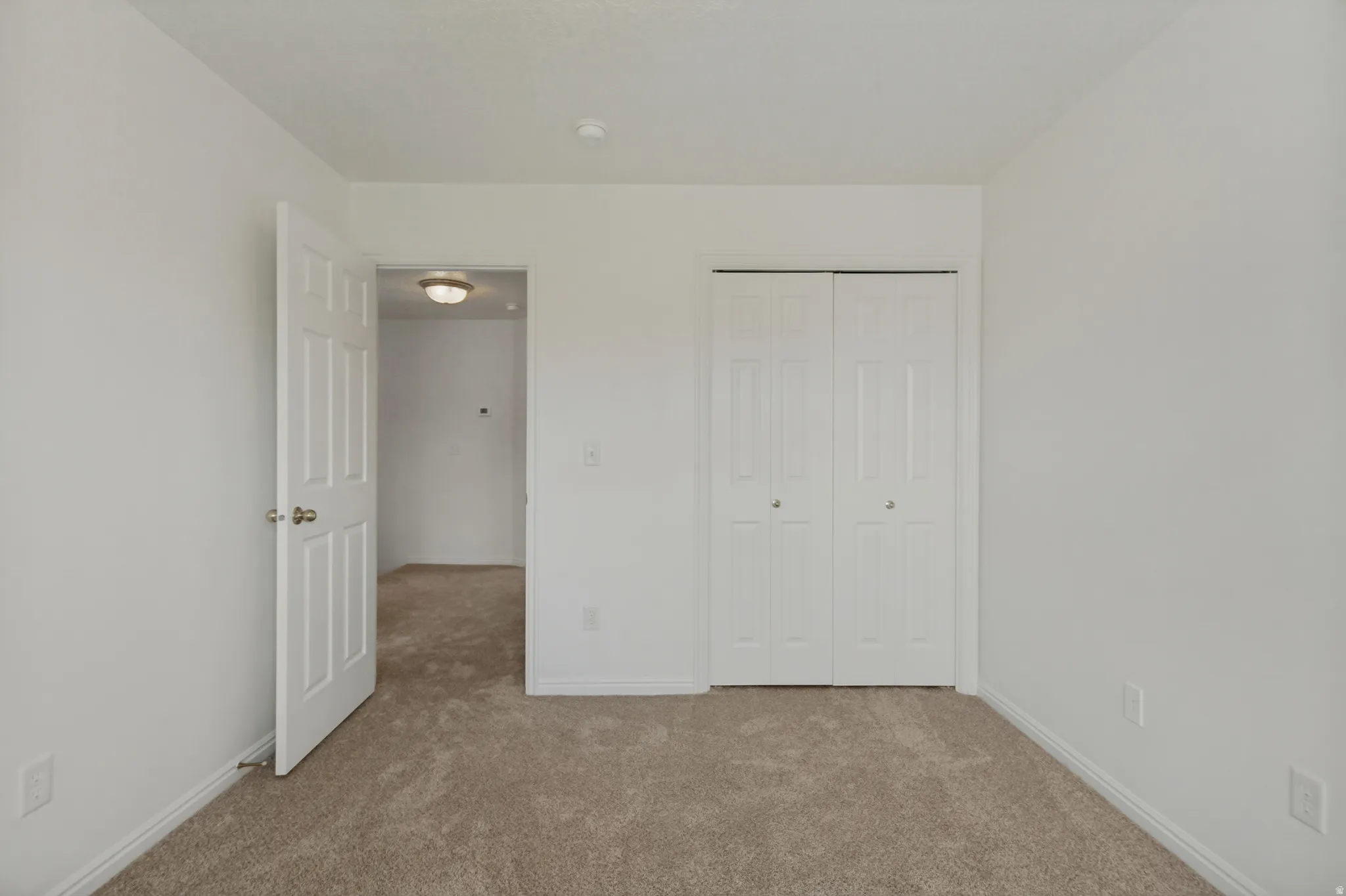Wall-to-wall carpeting in a neutral tone, white bi-fold closet doors, and a white paneled interior door