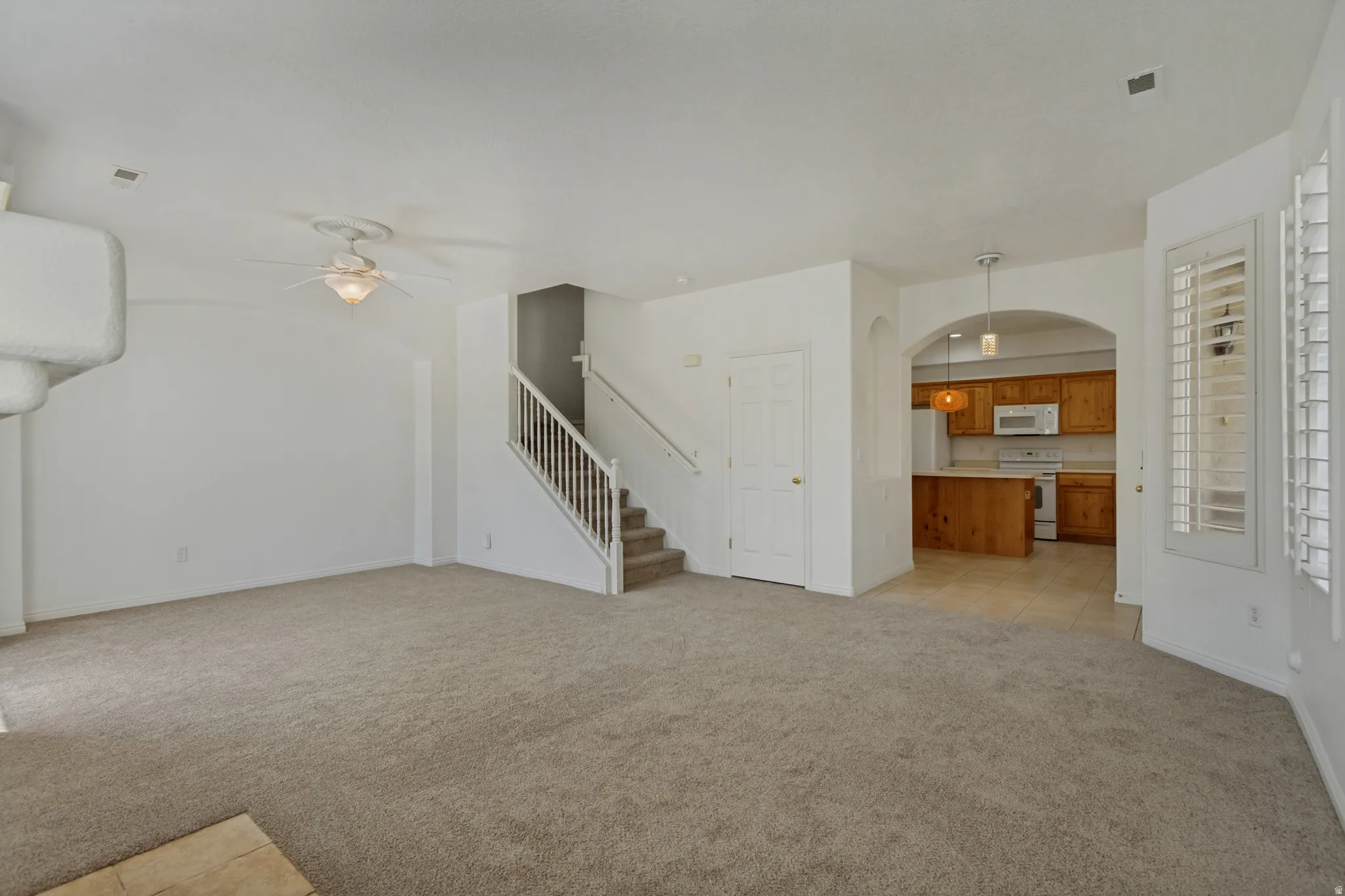 Carpeted living area featuring an architectural fireplace element, ceiling fan, and a staircase with white balusters