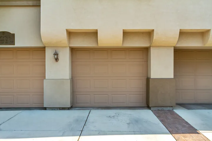 Stucco exterior with panel garage doors, concrete driveway, and exterior lighting