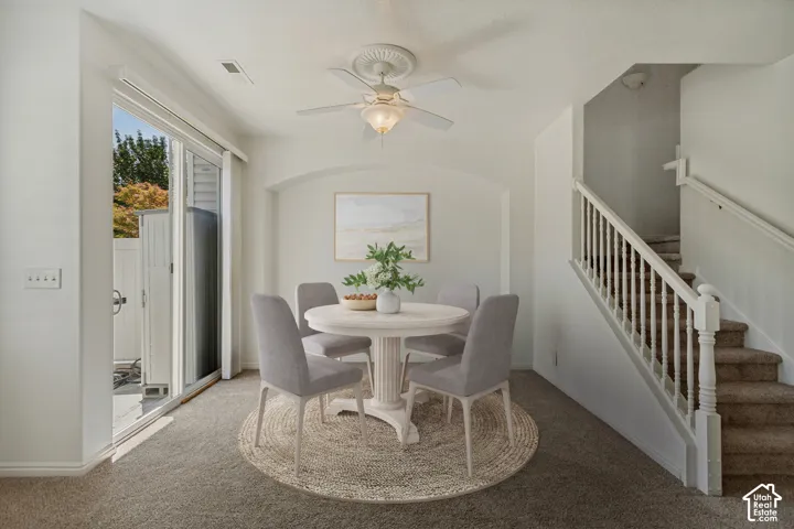 Sliding glass door, wall-to-wall carpeting, staircase with white banister, archway, and ceiling fan with integrated lighting