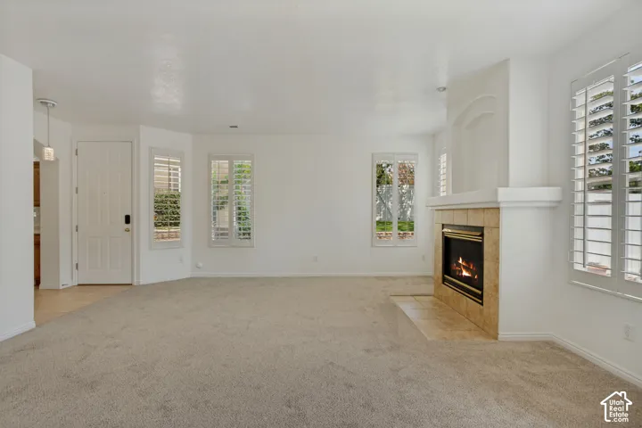 Neutral carpet flooring, fireplace with tile surround, multiple windows with plantation shutters, and a paneled entry door