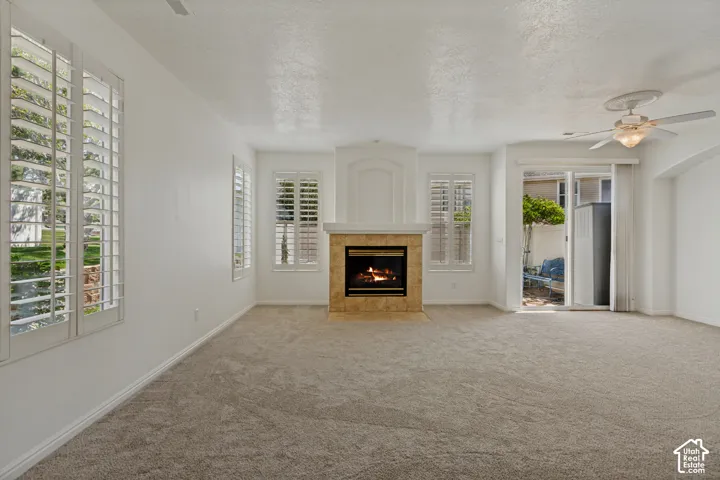 Carpeted living area featuring a fireplace with a tile surround, plantation shutters on multiple windows, a ceiling fan, and a sliding glass door