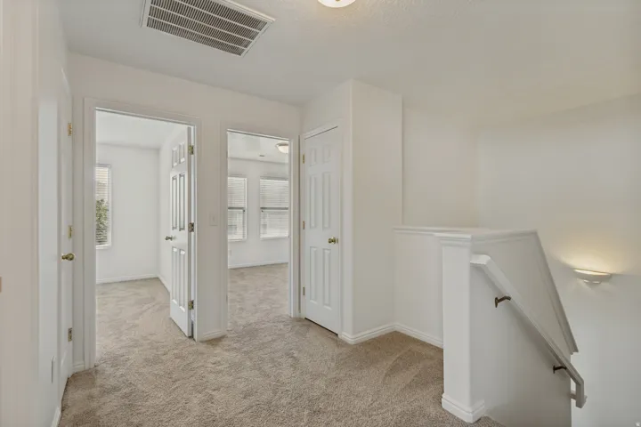 Carpeted hallway with white interior doors, a staircase with a white railing, and a wall-mounted light fixture