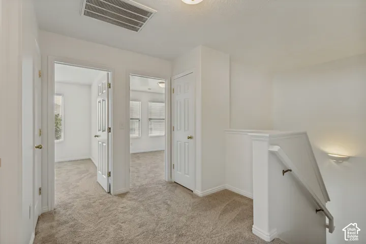 Carpeted hallway with white interior doors, a staircase with a white railing, and a wall-mounted light fixture