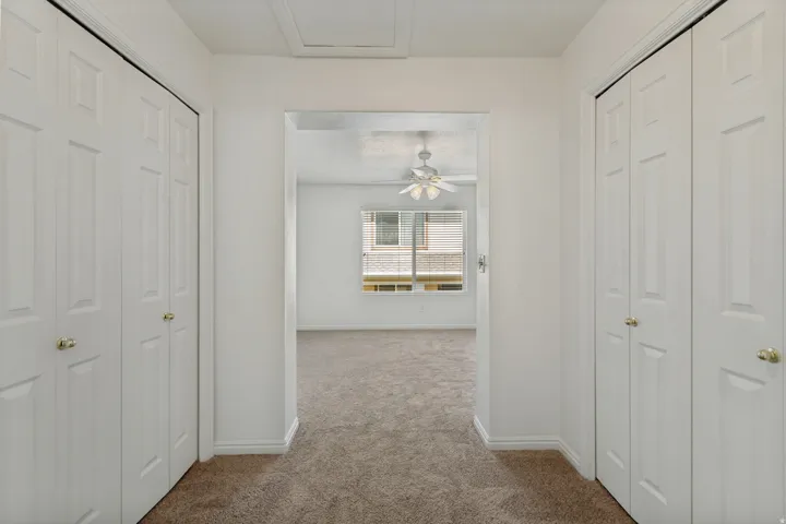 Plush carpet flooring, white bi-fold closet doors, brass door hardware, white window blinds, and a ceiling fan with integrated lighting