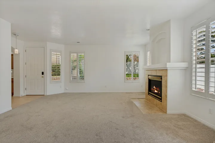 Neutral carpet flooring, fireplace with tile surround, multiple windows with plantation shutters, and a paneled entry door