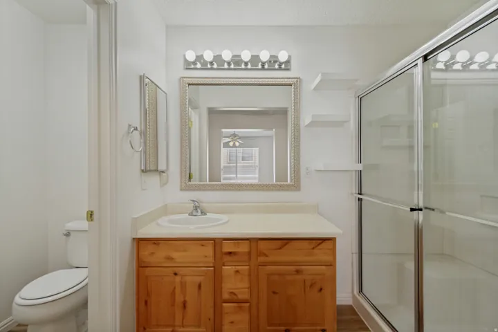 Vanity with integrated sink, natural wood-finish cabinetry, and framed mirror