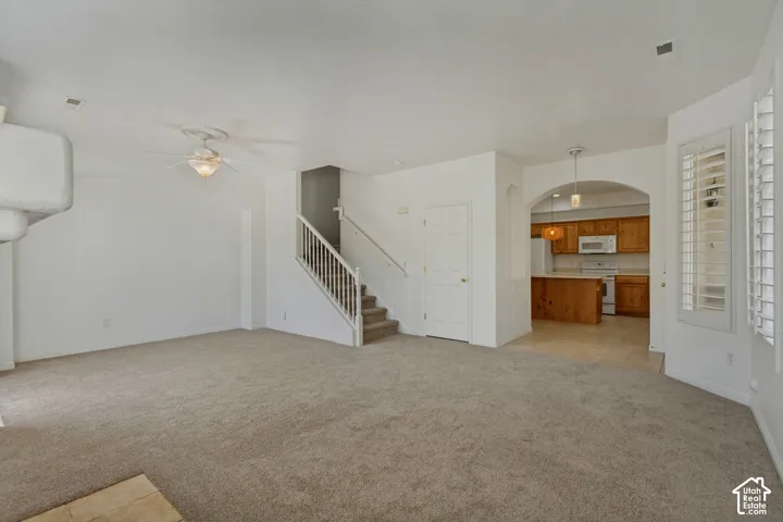 Carpeted living area featuring an architectural fireplace element, ceiling fan, and a staircase with white balusters