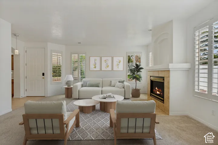 Light-filled living area featuring a built-in fireplace with stone-finish surround, multiple windows with plantation shutters, and light-toned carpet flooring