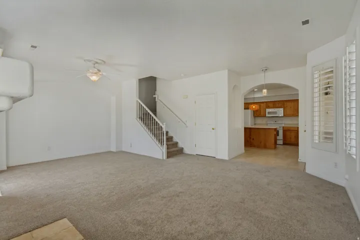 Carpeted living area featuring an architectural fireplace element, ceiling fan, and a staircase with white balusters