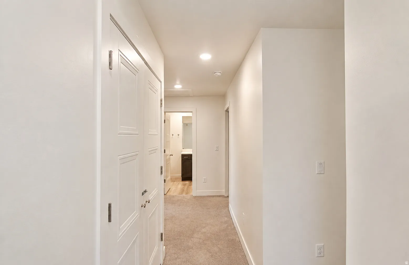 Recessed lighting illuminates a hallway with carpet flooring and white walls